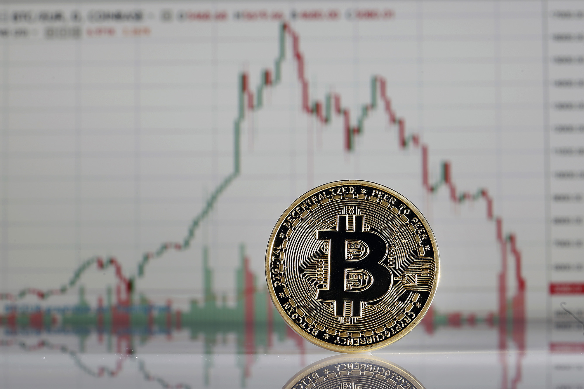 In this photo illustration, a visual representation of a Bitcoin is displayed in front of a line graph of Bitcoin prices