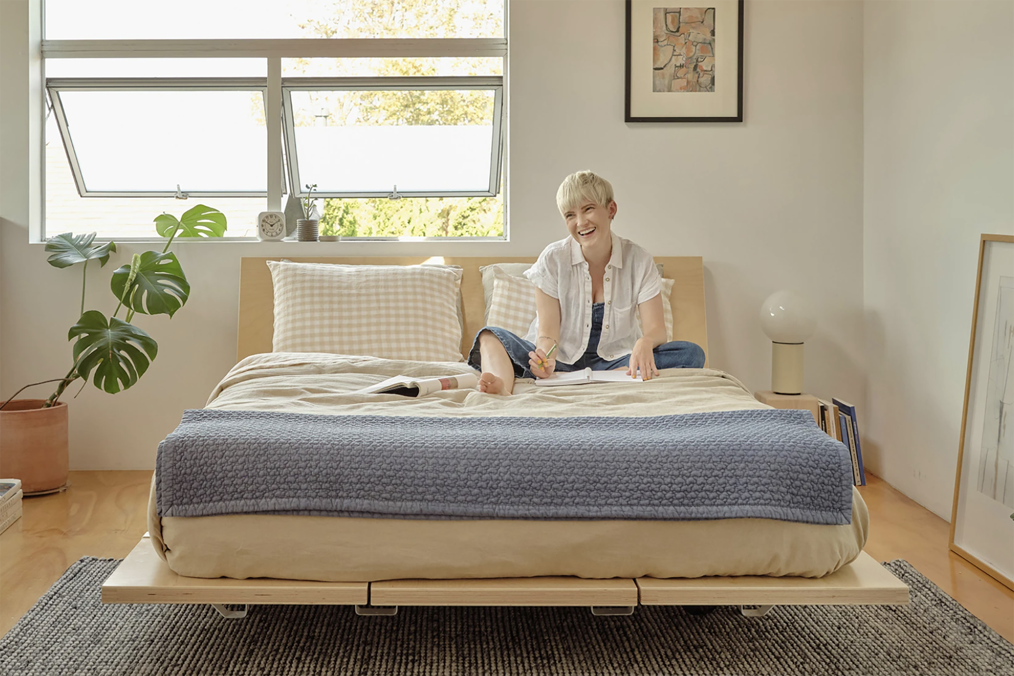 A woman sits on a bed in a well-lit bedroom