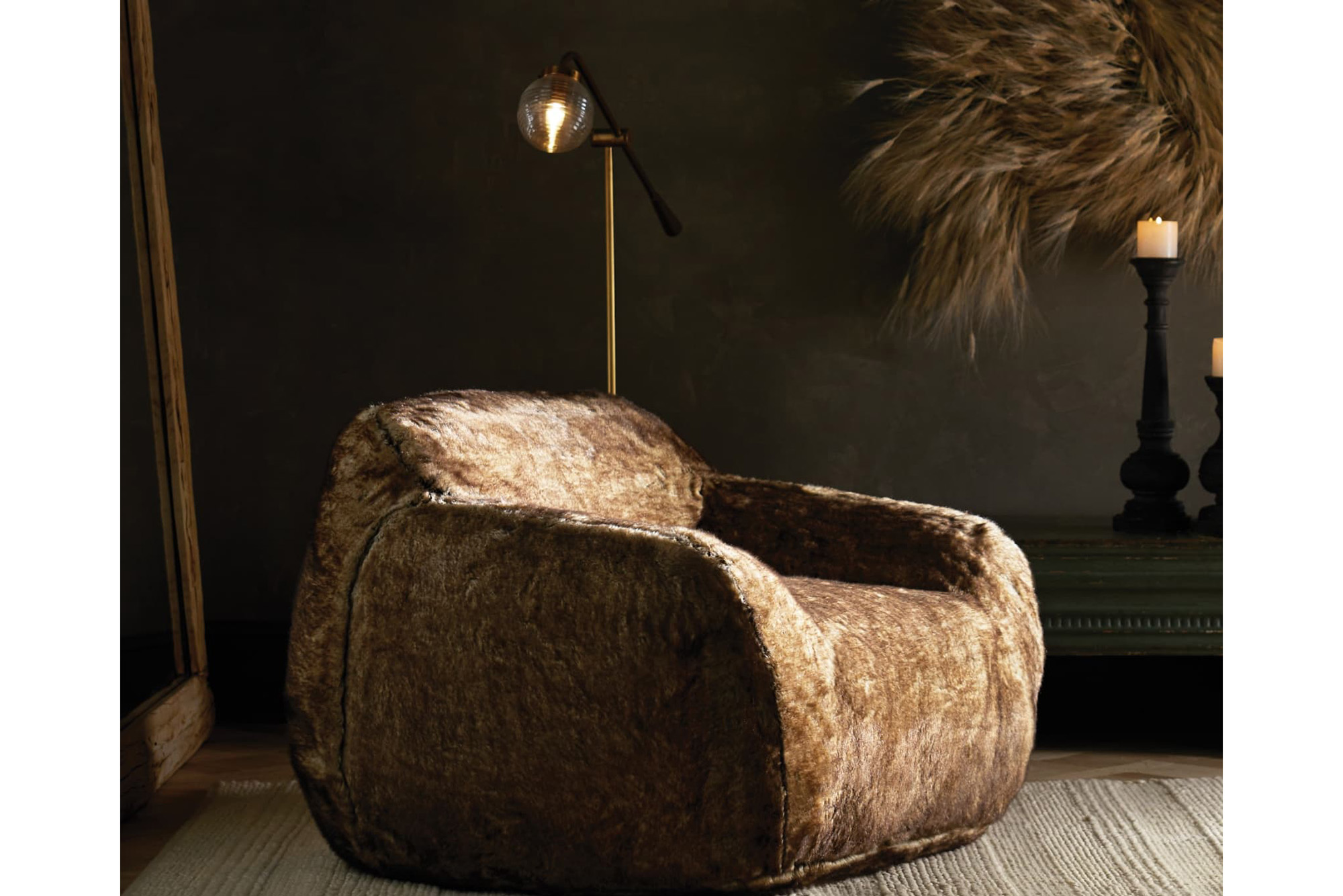 A dark brown loveseat chair in a dark colored living room with a gold lamp