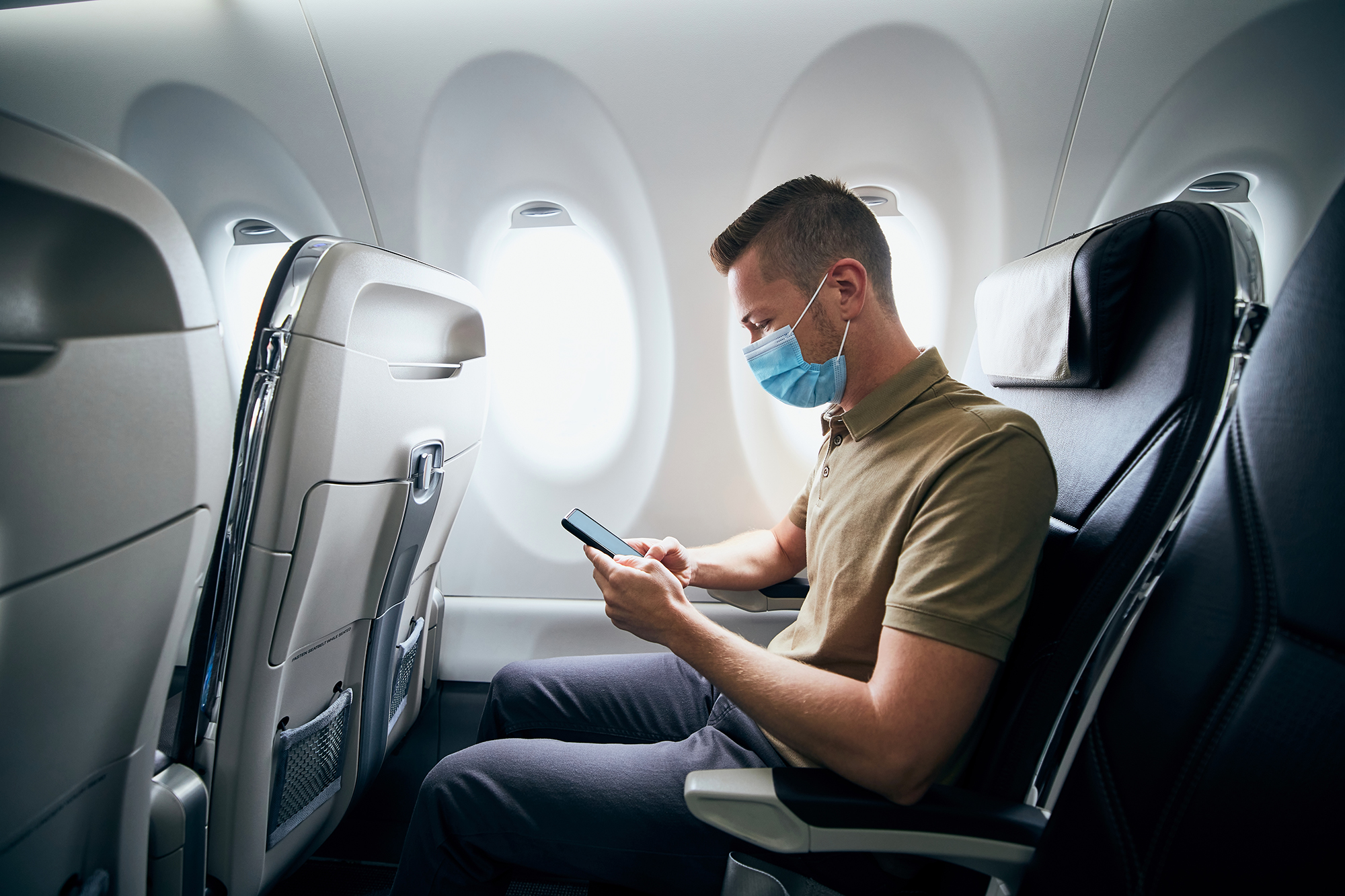 Man wearing face mask and using phone inside airplane during flight.